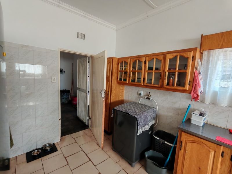 A functional laundry room featuring tiled flooring, wall-mounted wooden cabinetry, and a tiled splashback with dedicated plumbing connections.