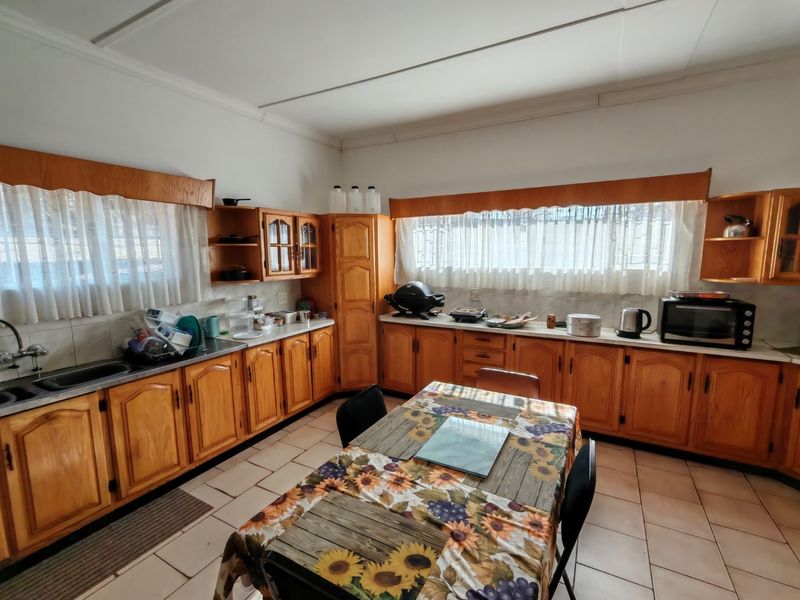 A spacious farm-style kitchen featuring extensive wooden cabinetry, laminate countertops, a double basin sink, and tiled flooring with a functional layout.