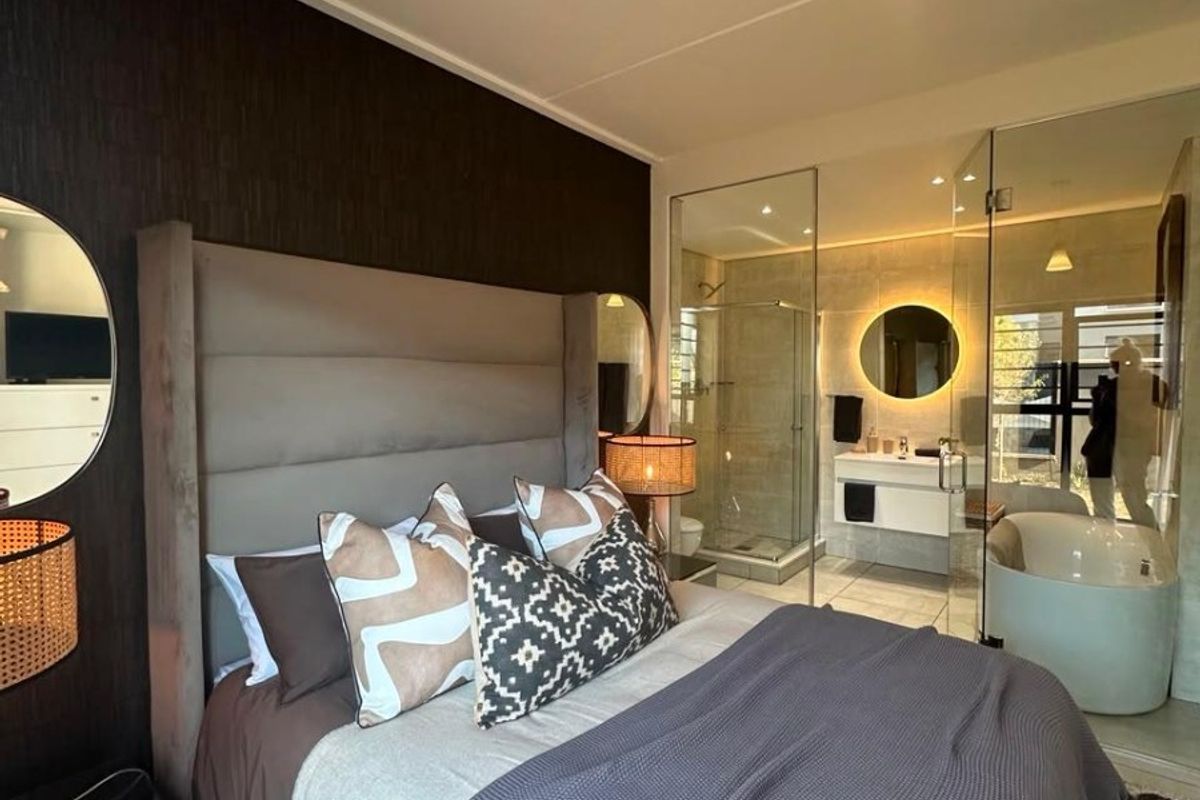 Modern bedroom featuring a contemporary glass-enclosed ensuite bathroom with a freestanding bathtub, walk-in shower, and sleek wall-mounted vanity.