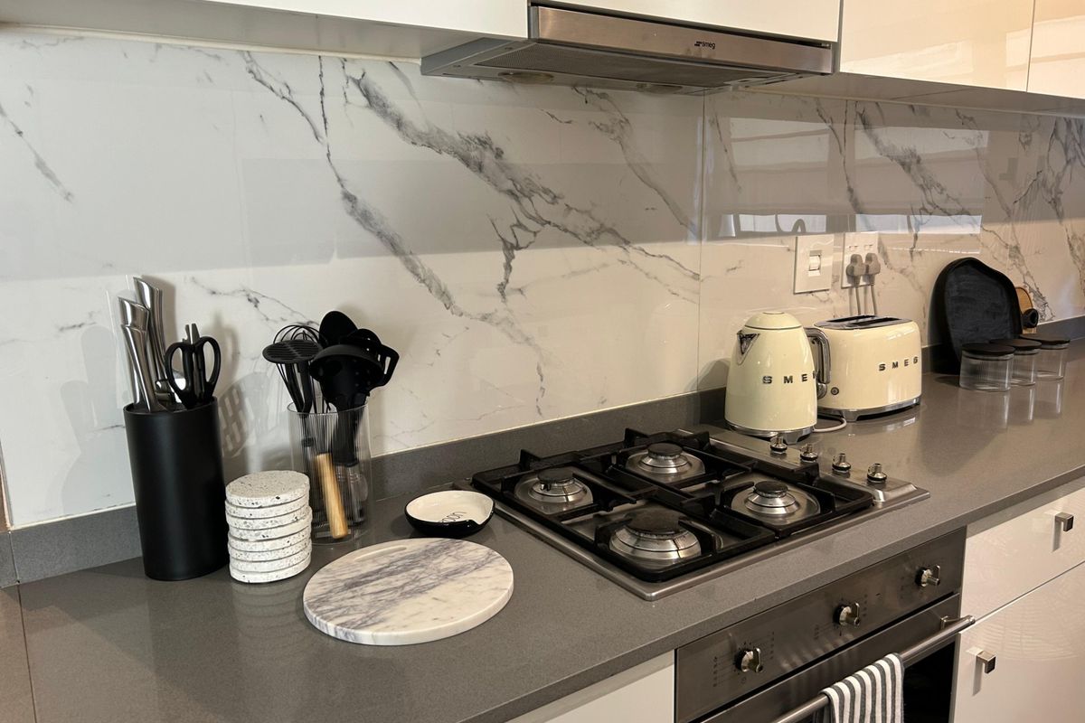 Modern kitchen featuring a gas hob, built-in oven, extractor fan, stone countertops, and a stylish marble-look splashback.