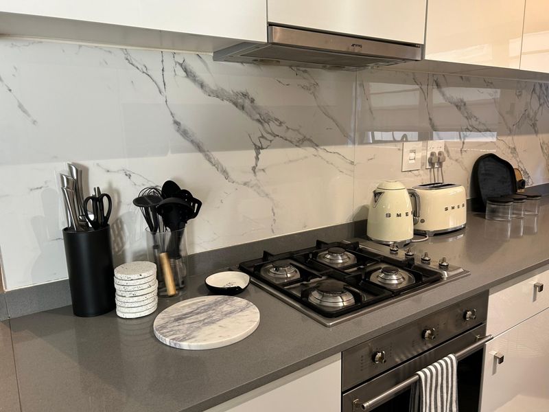 Modern kitchen featuring a gas hob, built-in oven, extractor fan, stone countertops, and a stylish marble-look splashback.