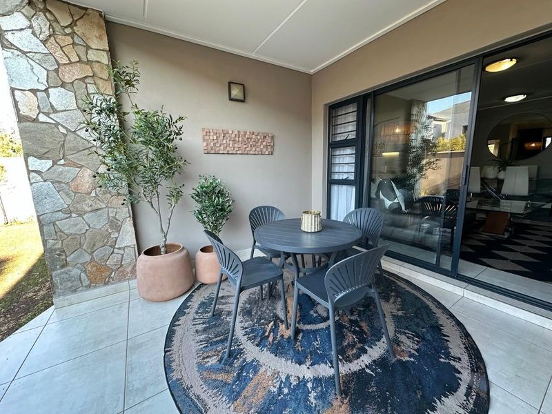 A covered patio area featuring tiled flooring, a decorative stone-clad feature wall, and large sliding glass doors providing access to the interior living space.