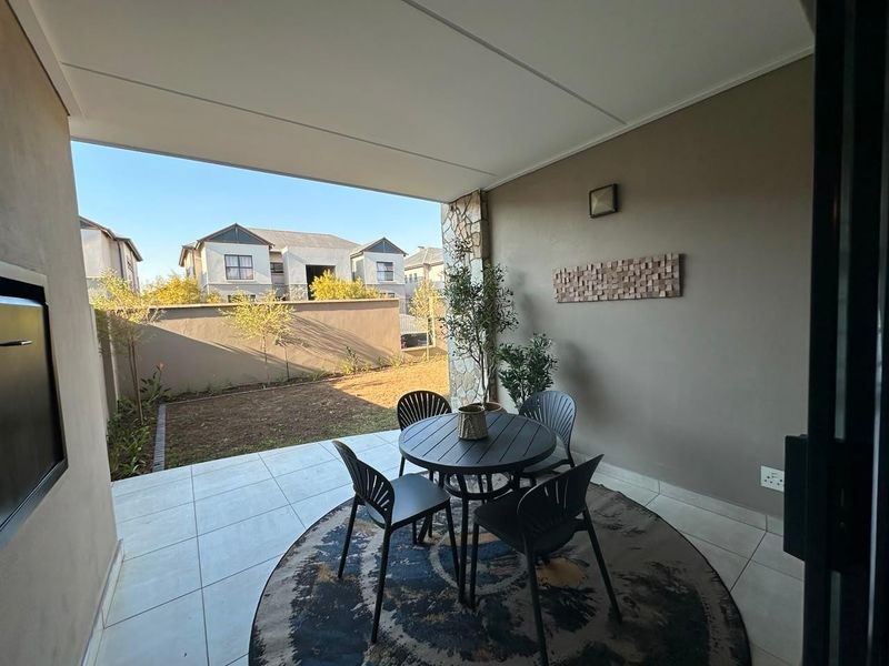A covered patio featuring tiled flooring, a built-in braai, and a stone-clad pillar, overlooking a private garden area.