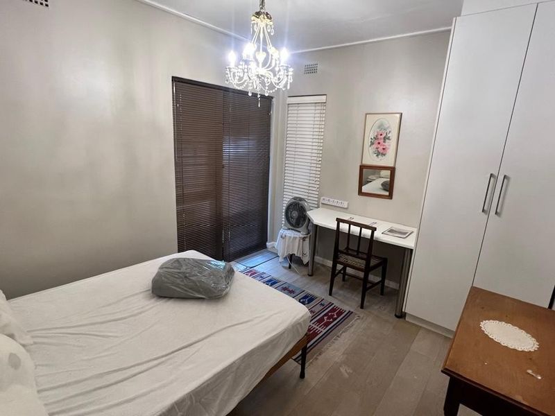 A functional bedroom featuring built-in wardrobes, laminate flooring, and venetian blinds, offering a neutral space ready for personalization.