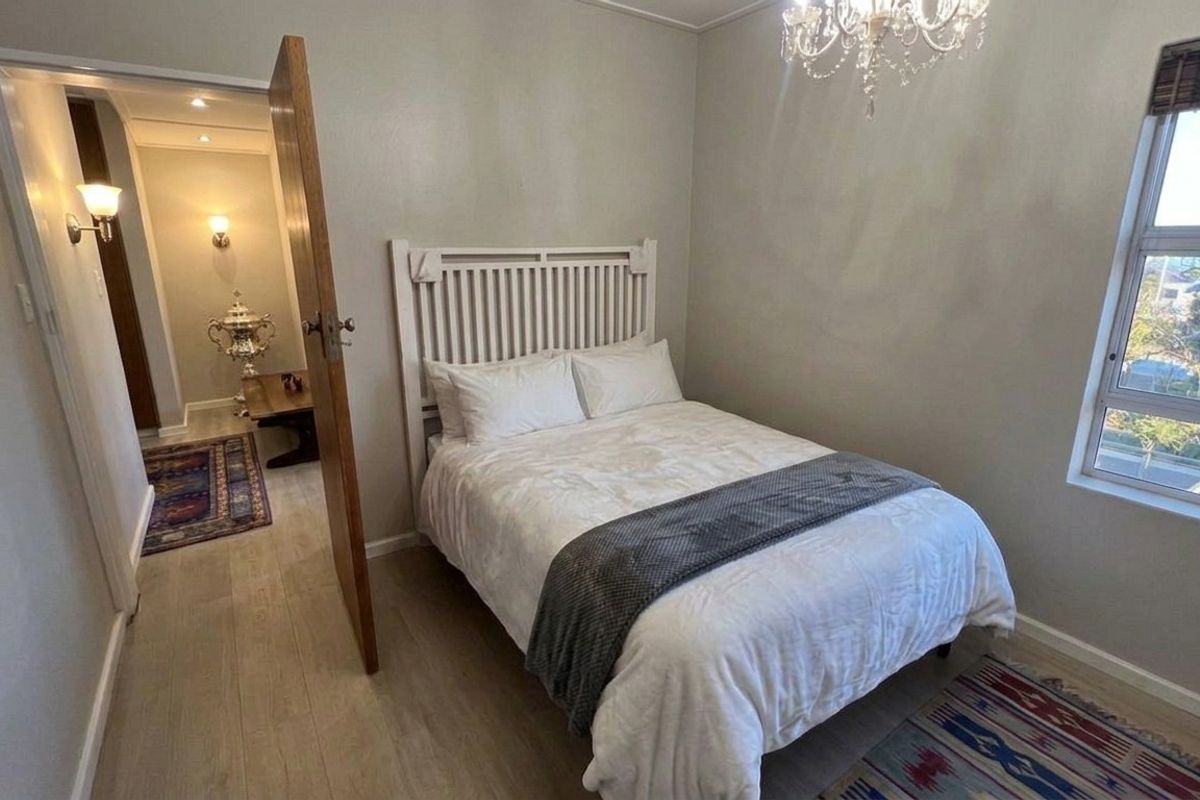 A well-maintained bedroom featuring neutral wall tones, laminate flooring, a classic chandelier, and a window providing natural light.