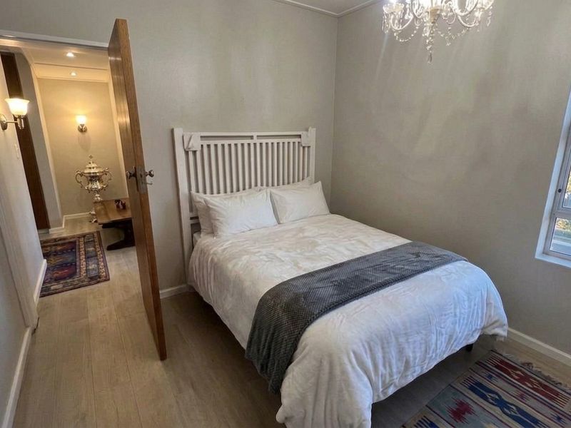 A well-maintained bedroom featuring neutral wall tones, laminate flooring, a classic chandelier, and a window providing natural light.