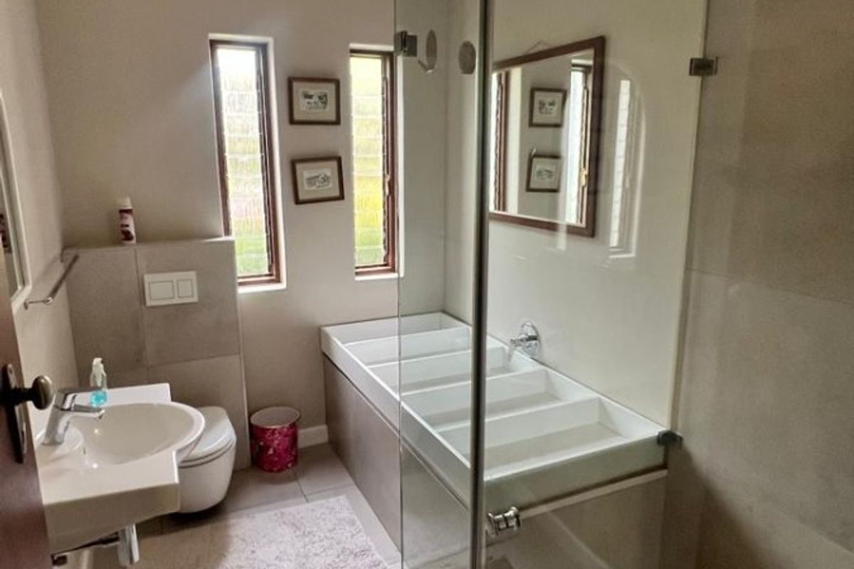 A modern bathroom featuring a wall-mounted basin, a toilet with a concealed cistern, and a glass-enclosed shower with tiled finishes.