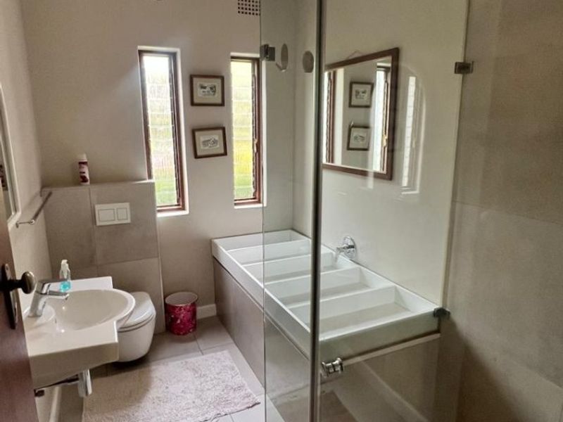 A modern bathroom featuring a wall-mounted basin, a toilet with a concealed cistern, and a glass-enclosed shower with tiled finishes.