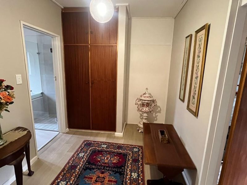 A functional hallway featuring built-in wooden storage cabinetry and light-toned laminate flooring, providing access to an adjacent bathroom.