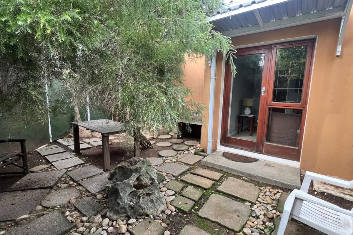 A rear garden area featuring stone paving, pebble landscaping, and a timber-framed glass door providing access to the interior.
