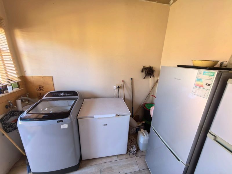 A functional laundry area featuring tiled flooring and a tiled splashback, providing a practical space for utility and appliance storage.