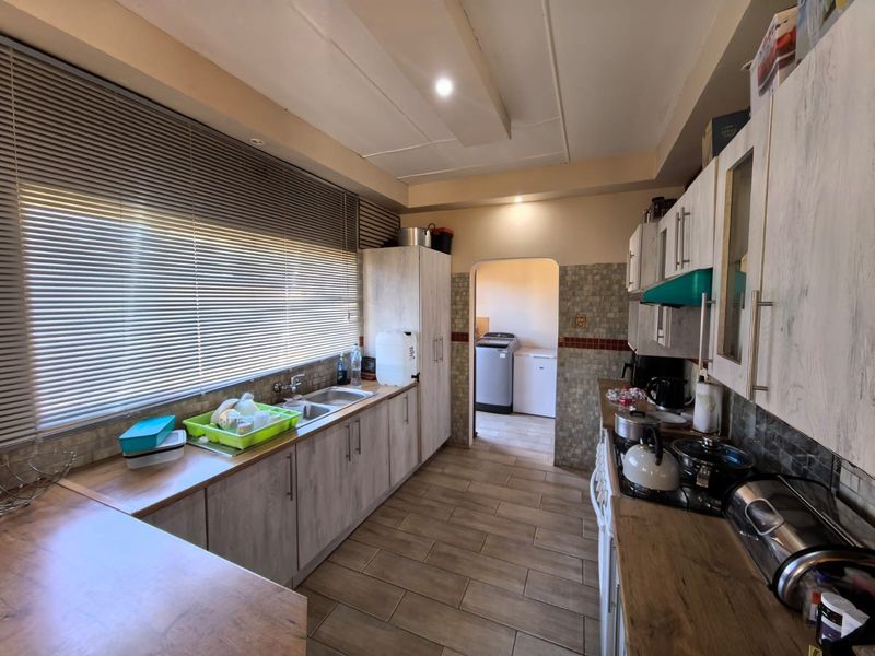 A functional kitchen featuring wood-look cabinetry, laminate countertops, tiled backsplash, and a dedicated scullery area visible through the arched doorway.