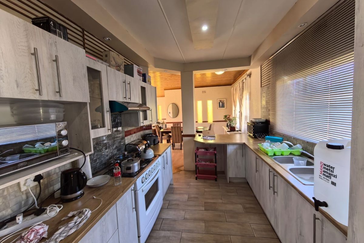 A functional kitchen featuring light wood-grain cabinetry, laminate countertops, a double sink, and a freestanding oven, with an open-plan flow to the dining area.