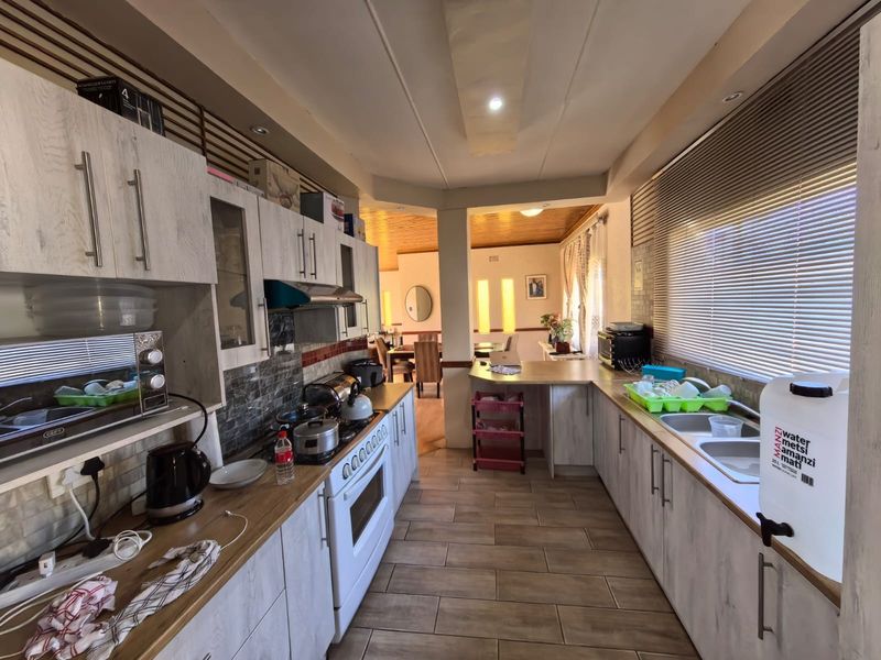 A functional kitchen featuring light wood-grain cabinetry, laminate countertops, a double sink, and a freestanding oven, with an open-plan flow to the dining area.