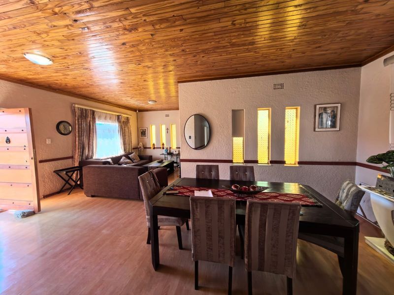 Spacious open-plan living and dining area featuring a warm timber ceiling, laminate flooring, and unique vertical feature windows.