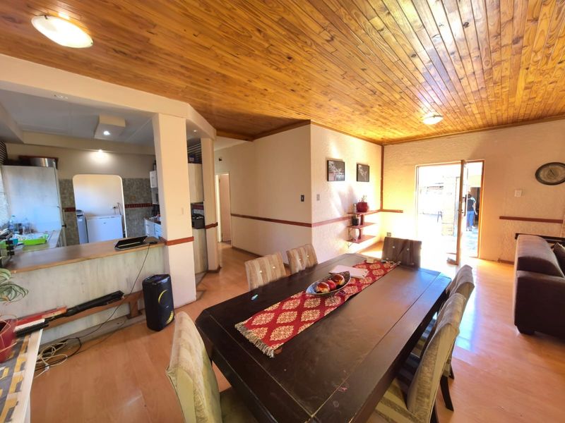 Open plan living and dining area featuring a wooden tongue and groove ceiling, laminate flooring, and an adjoining kitchen with a breakfast counter.