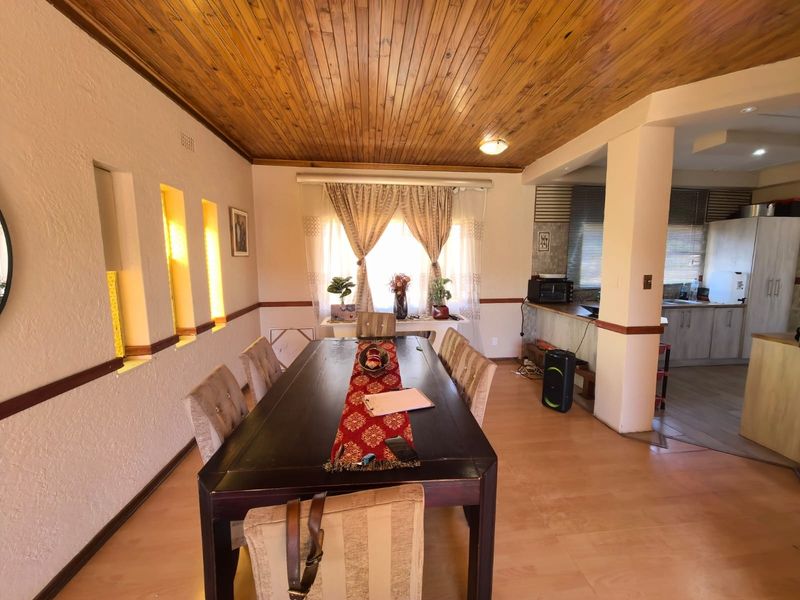 Open-plan dining area featuring a timber ceiling and laminate flooring, seamlessly flowing into a functional kitchen with built-in cabinetry and a breakfast bar.