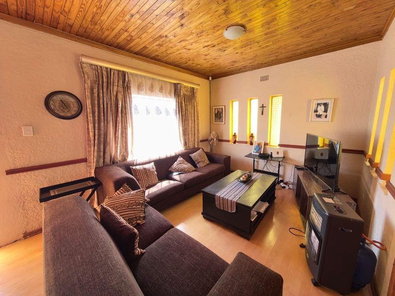 A cozy living room featuring a warm timber tongue and groove ceiling, laminate flooring, and unique vertical slit windows.