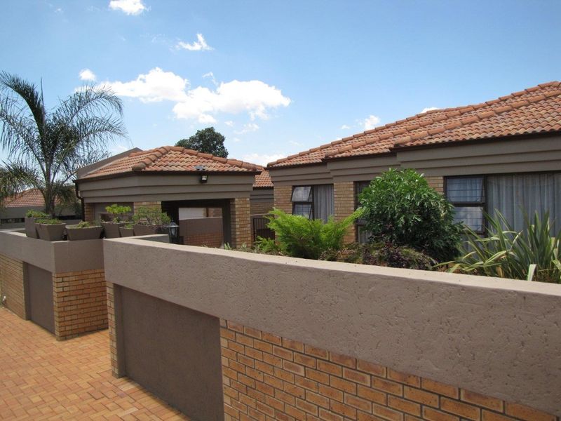 A well-maintained residential exterior featuring a brick facade, tiled roof, and paved driveway with established boundary walls and landscaping.