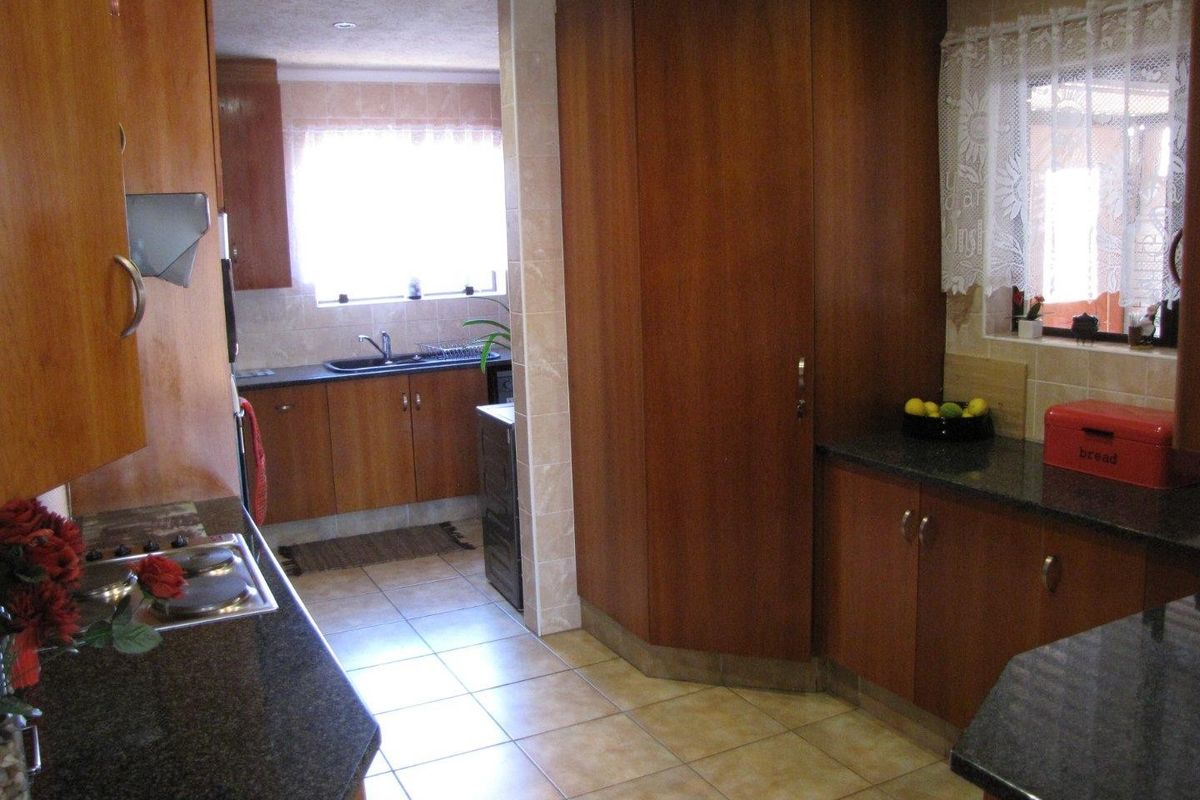 A functional kitchen featuring wood-finish cabinetry, dark granite countertops, ceramic tile flooring, and a built-in hob with a tiled backsplash.