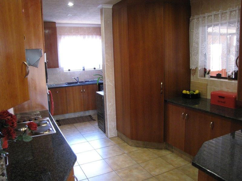 A functional kitchen featuring wood-finish cabinetry, dark granite countertops, ceramic tile flooring, and a built-in hob with a tiled backsplash.
