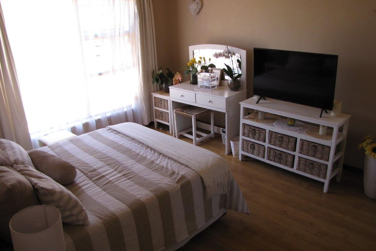 A cozy bedroom featuring light-toned laminate flooring and a large sliding window that allows for natural light.
