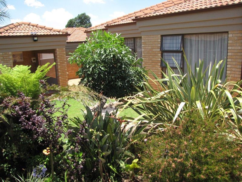 A view of the rear garden featuring a well-maintained face brick exterior, tiled roof, and established landscaping.