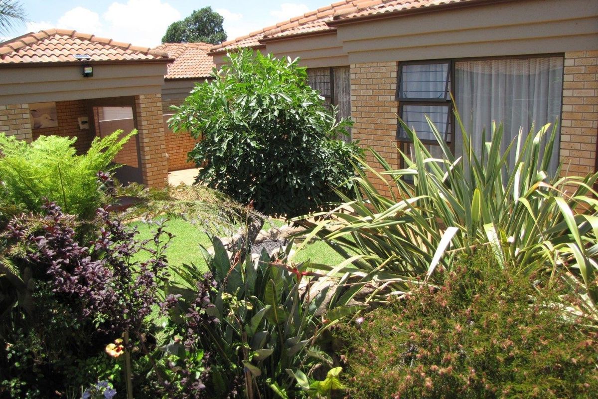 A view of the rear garden featuring a well-maintained face brick exterior, tiled roof, and established landscaping.