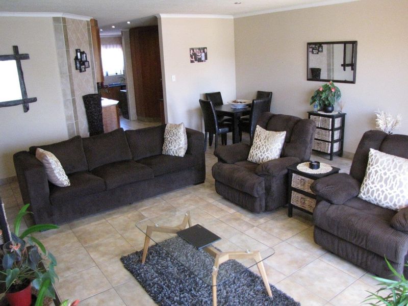 An open-plan living and dining area featuring neutral tiled flooring, recessed lighting, and a tiled feature pillar, connecting to the kitchen space.
