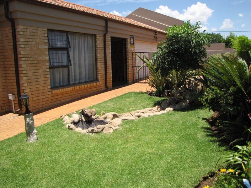 Front view of a face brick house featuring a paved walkway, security gate, and a well-maintained garden with a decorative rock feature.