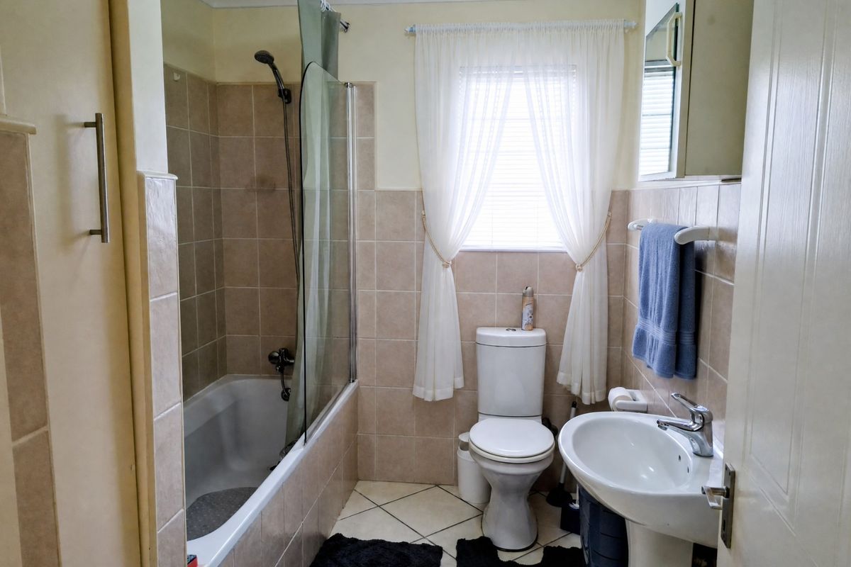 A functional bathroom featuring a bathtub with a glass shower screen, a pedestal basin, and a toilet, finished with neutral wall and floor tiles.