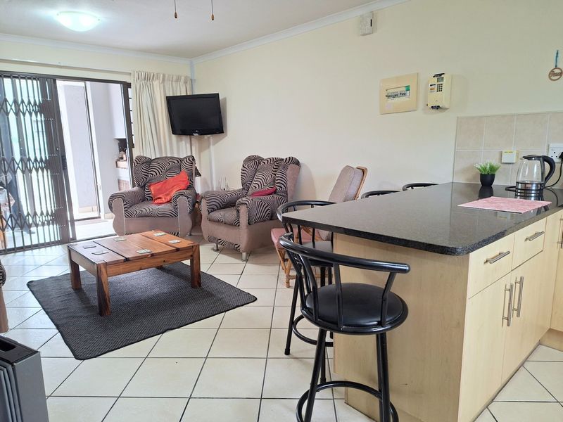 Open-plan living area featuring a kitchen island with granite countertops, tiled flooring, and direct access to a patio through a sliding security gate.