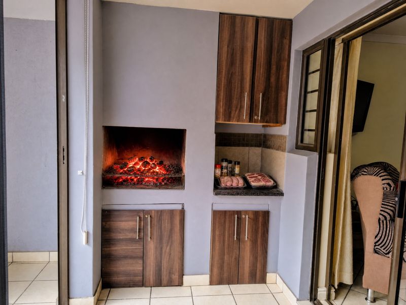 Covered patio area featuring a built-in braai, wood-look cabinetry, granite prep surface, and tiled flooring, ideal for outdoor entertaining.