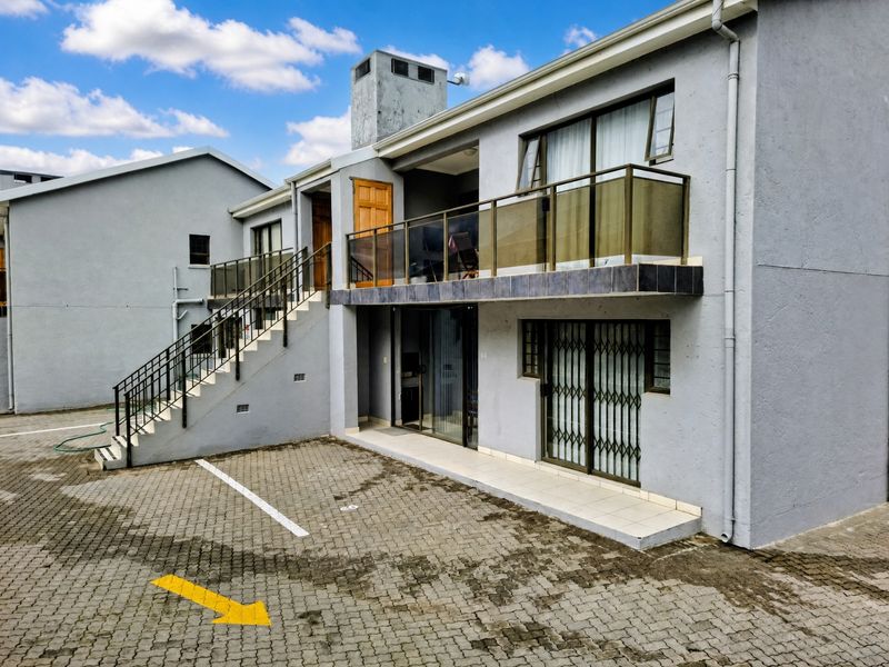 Exterior view of an apartment building featuring a paved parking area, external staircase, and a balcony with glass balustrades.