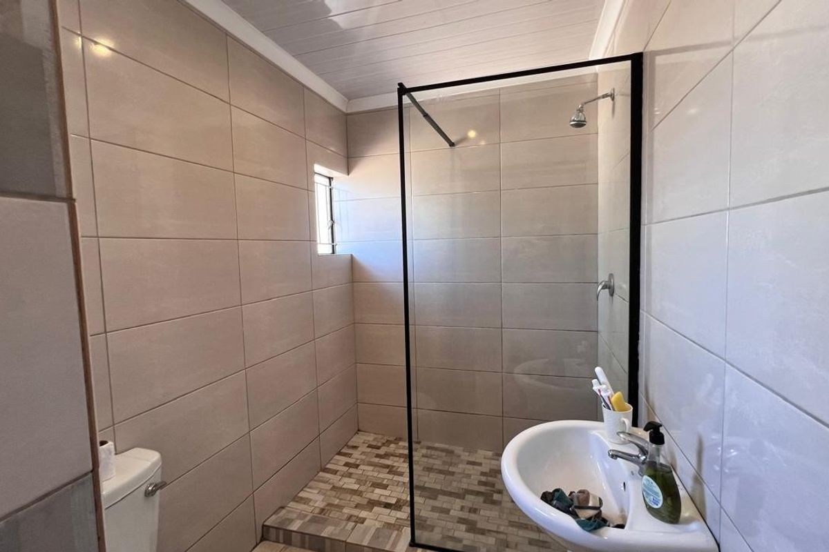 Modern bathroom featuring a walk-in shower with a black-framed glass screen, pedestal basin, and neutral ceramic wall tiling.
