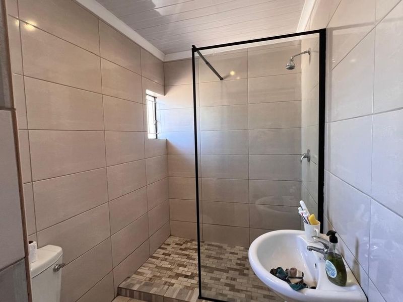Modern bathroom featuring a walk-in shower with a black-framed glass screen, pedestal basin, and neutral ceramic wall tiling.