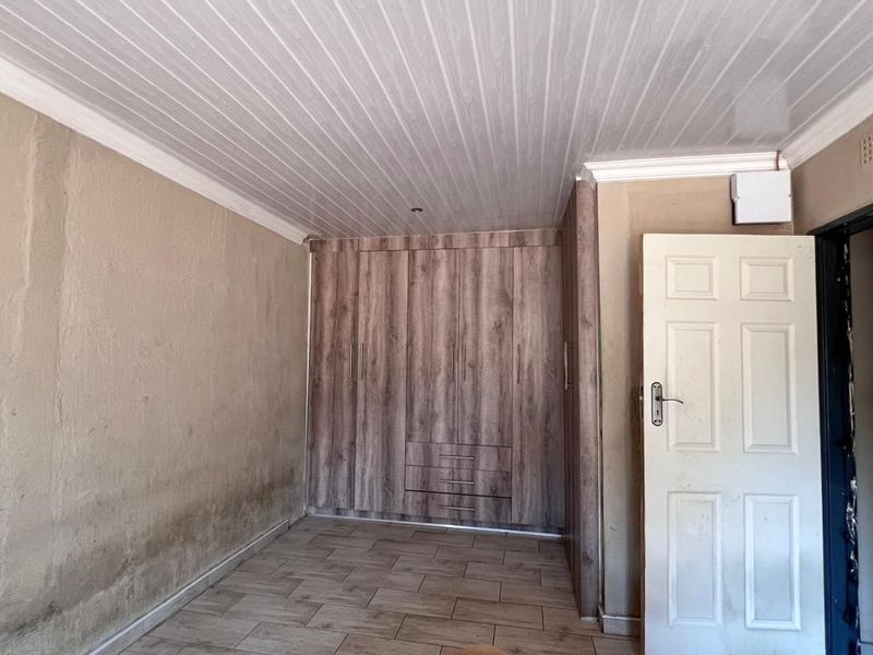 A bedroom featuring built-in cupboards, tiled flooring, and a PVC ceiling. The walls show signs of staining and require cosmetic attention.