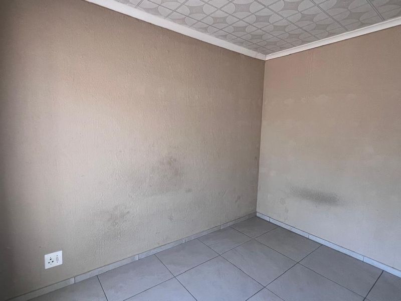 An empty bedroom featuring tiled flooring and patterned ceiling tiles, currently showing visible wall staining and signs of wear.