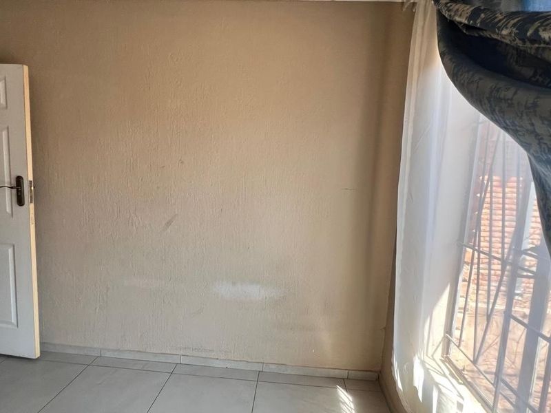 An empty bedroom featuring tiled flooring, a standard panel door, and security bars on the window, requiring minor cosmetic updates to the walls.