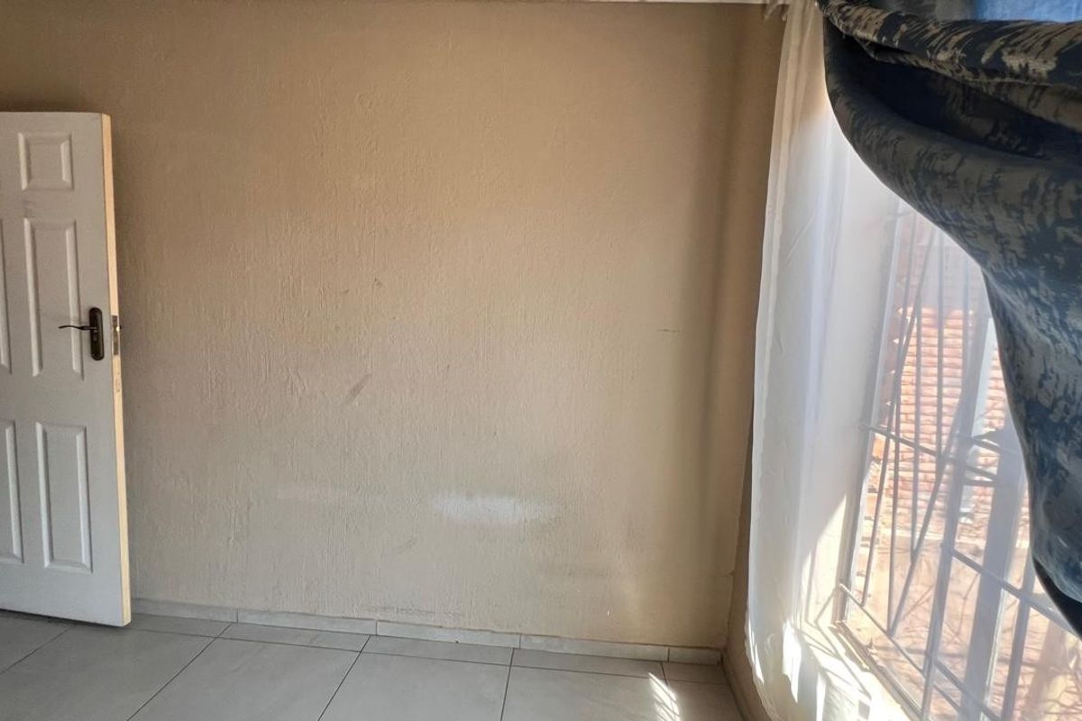 An empty bedroom featuring tiled flooring, a standard panel door, and security bars on the window, requiring minor cosmetic updates to the walls.