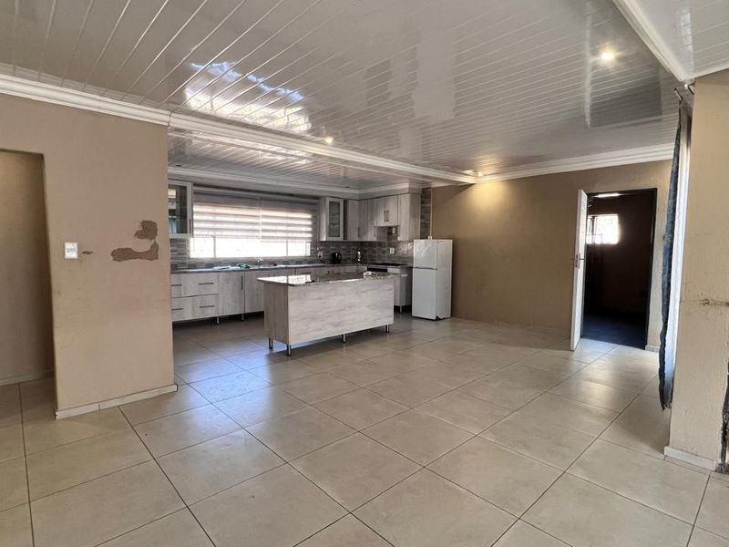 Open plan kitchen and living area featuring tiled floors, glossy ceiling panels, and a central kitchen island, currently in need of cosmetic repairs.