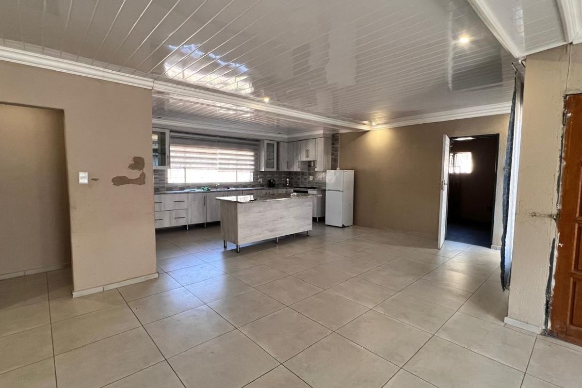 Open plan kitchen and living area featuring tiled floors, glossy ceiling panels, and a central kitchen island, currently in need of cosmetic repairs.