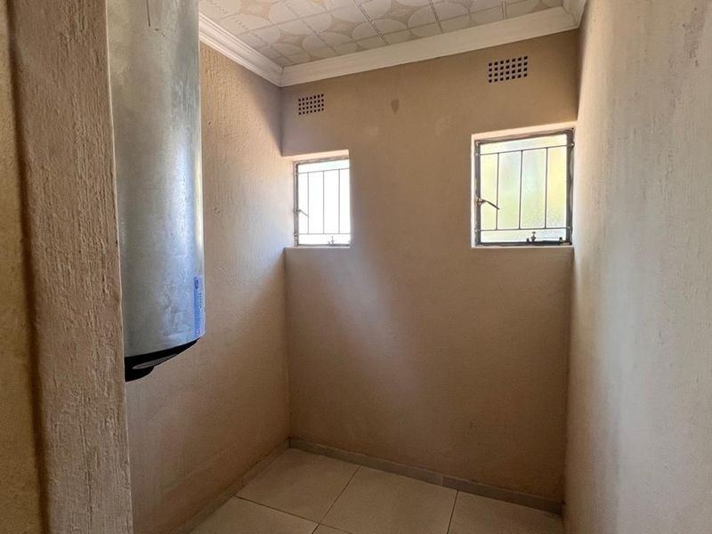 A functional utility space featuring tiled flooring, security-barred windows, and a wall-mounted electric geyser.