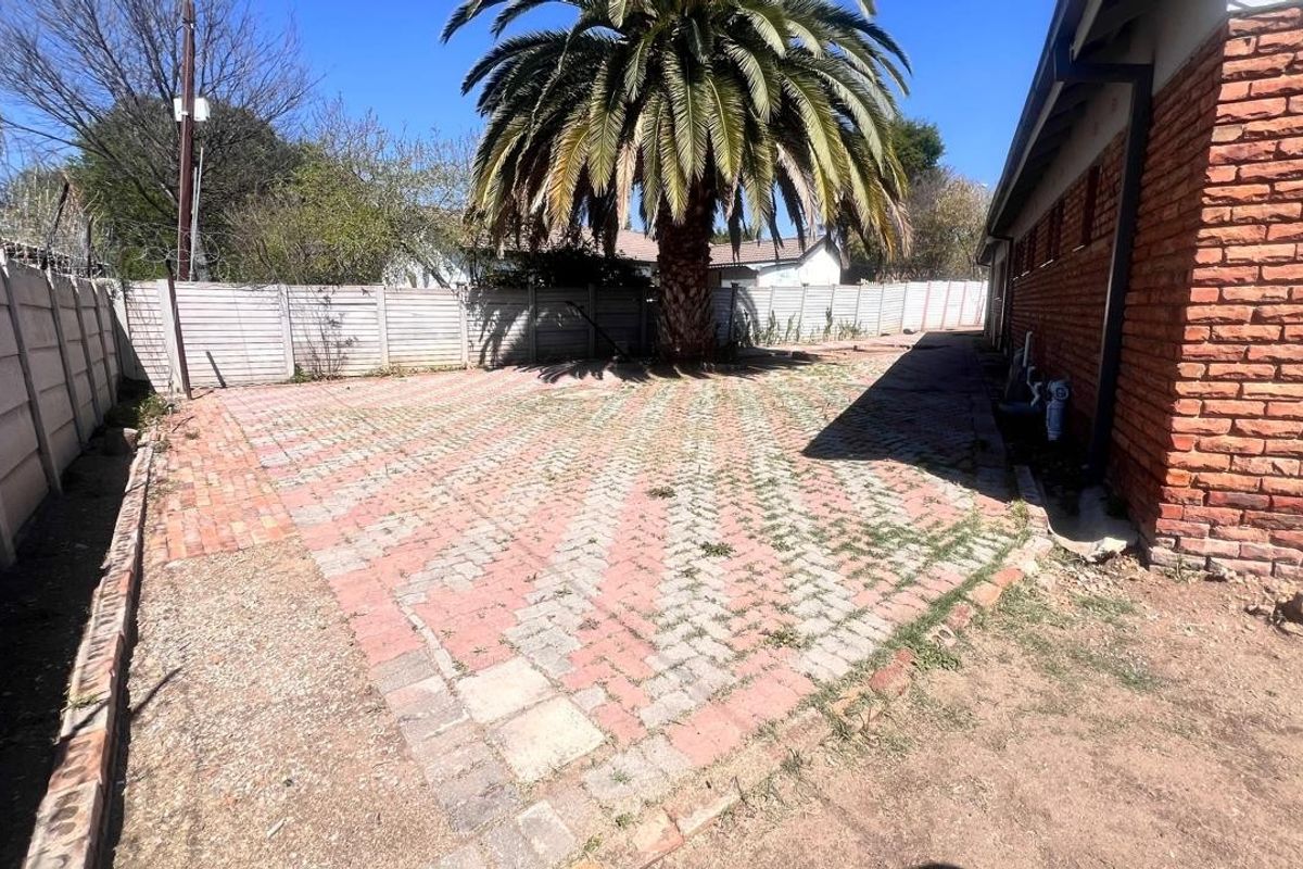 Rear exterior area featuring brick paving, a mature palm tree, and perimeter precast concrete walling alongside the brick house facade.