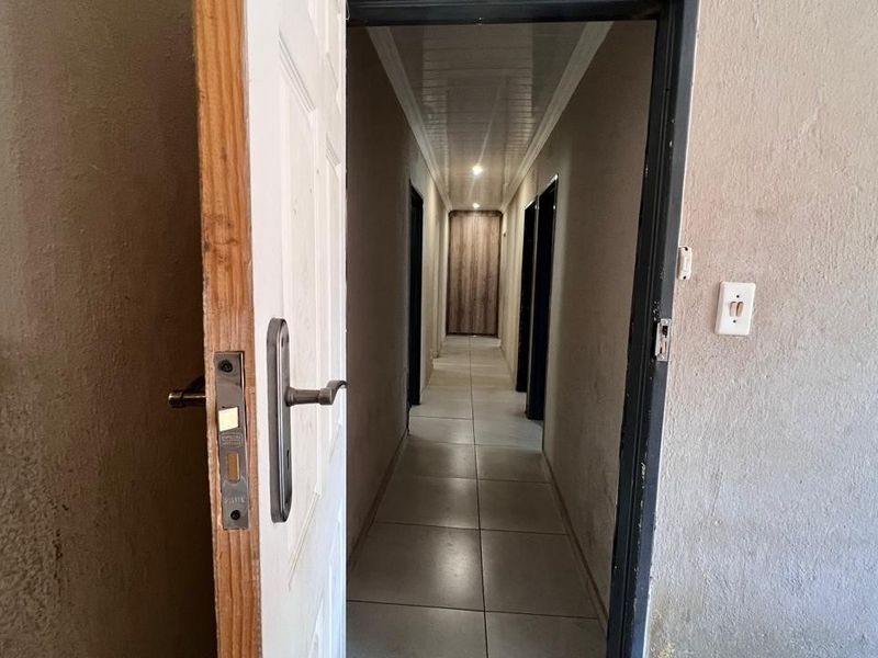 A narrow interior hallway featuring tiled flooring and recessed ceiling lighting, providing access to multiple rooms within the property.