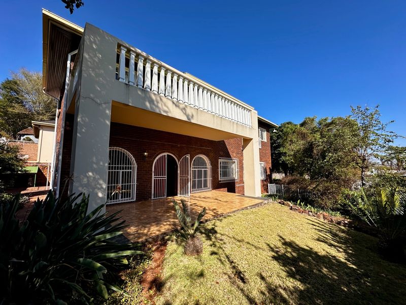 Rear view of the house featuring a covered tiled patio, brick facade, and an upper-level balcony with a balustrade.