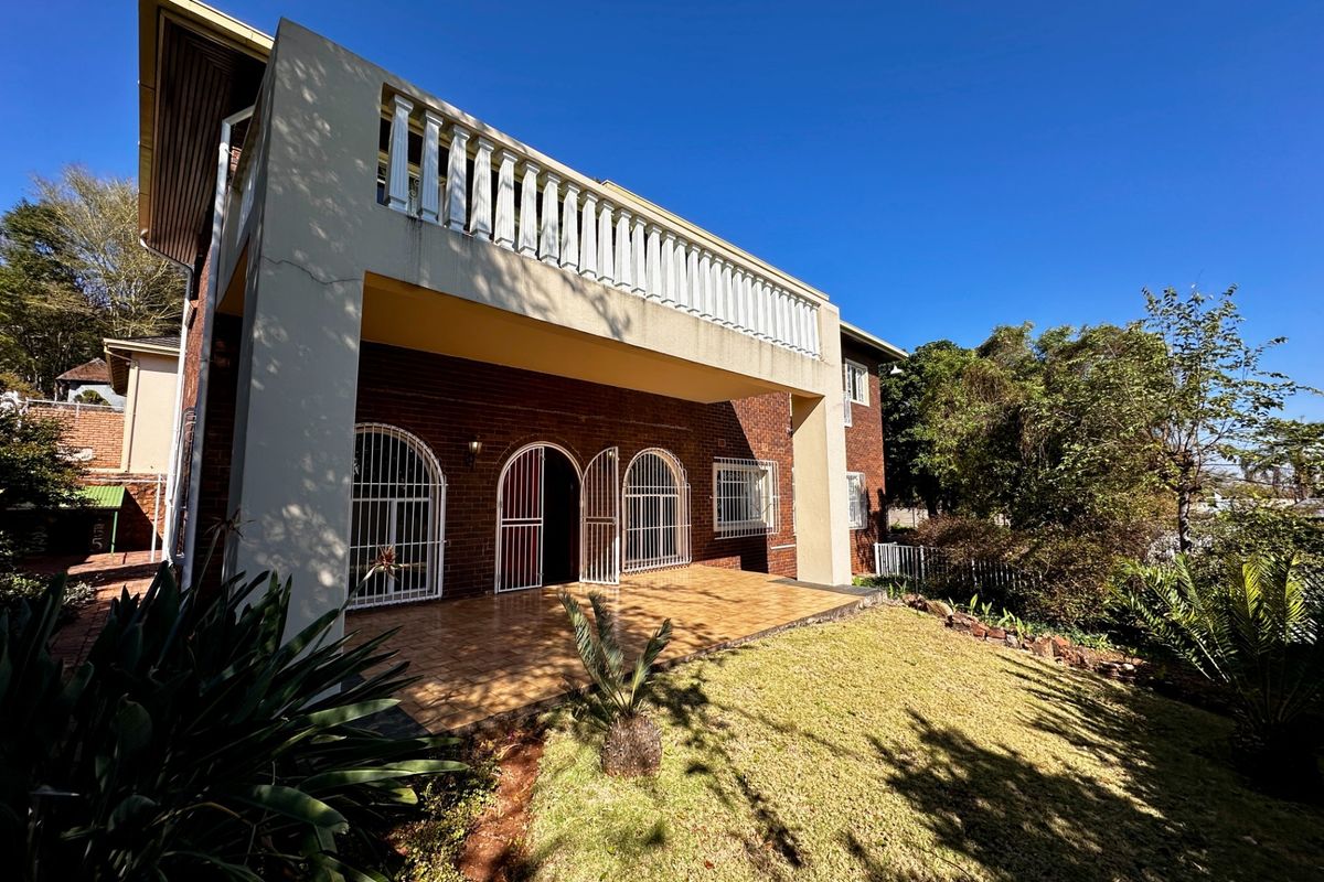 Rear view of the house featuring a covered tiled patio, brick facade, and an upper-level balcony with a balustrade.