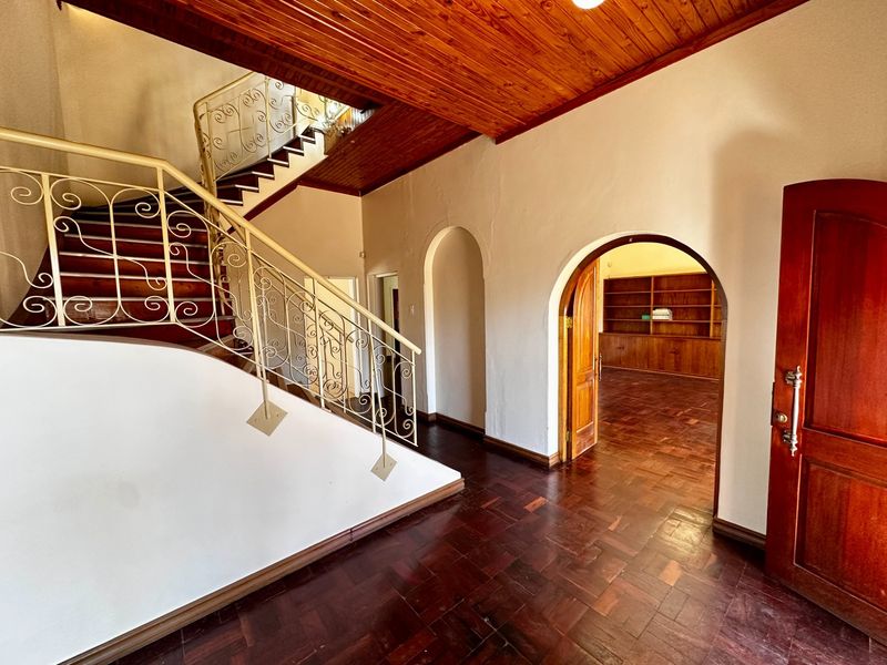 Spacious entrance hall featuring a grand wooden staircase with wrought iron balustrade, parquet flooring, and elegant arched doorways leading to adjacent rooms.