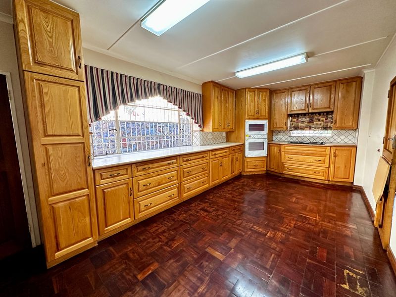 Spacious kitchen featuring extensive wooden cabinetry, built-in double oven, hob, tiled backsplash, and traditional parquet flooring.