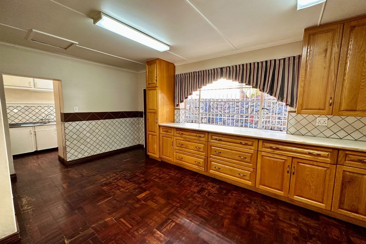 Spacious kitchen featuring traditional wooden cabinetry, parquet flooring, and a tiled splashback, with an adjacent scullery area visible through the doorway.